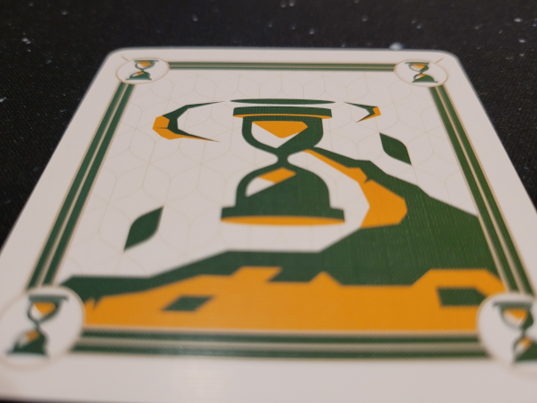 Nahaufnahme einer Jokerkarte auf der ein Wirbel und eine Sanduhr in Grün und Gelb zu sehen ist.