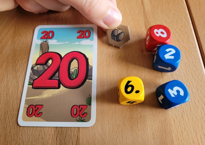 Eine Hand hält einen Gürteltier-Chips zwischen vier Würfel und eine Karte.