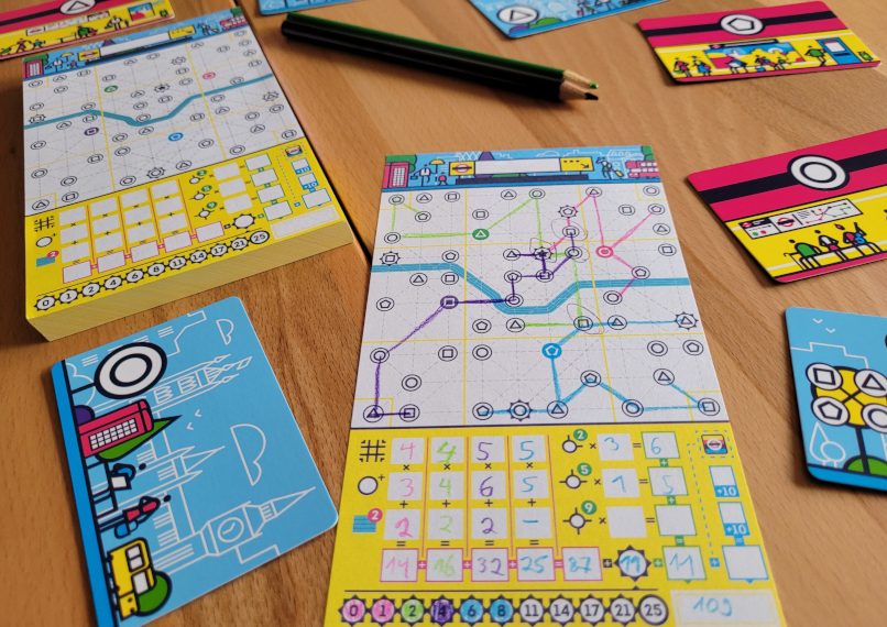 Spielmaterial von "Next Station London": Stifte, Karten, der Block und eine ausgefüllte Seite des Blocks.