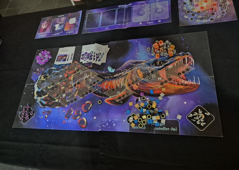 Ein Spielplan zeigt einen Aal, der aus einem Asteroiden geflogen kommt.
