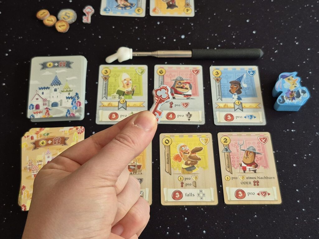 Eine Hand hält einen Schlüsselmarker über Spielmaterial.