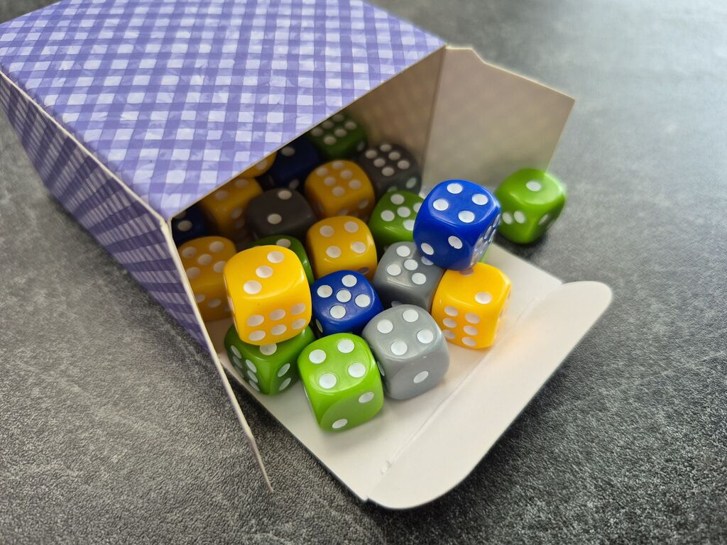 Würfel in grün, blau, gelb und grau kullern aus einer Schachtel.