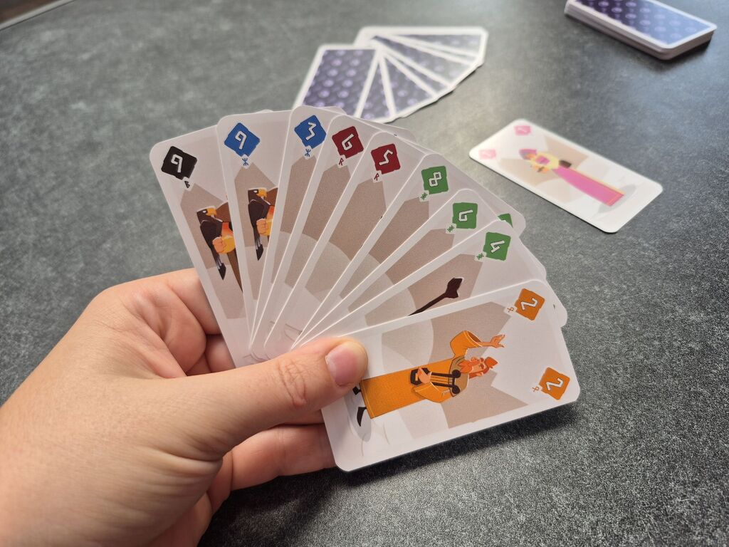 Eine Hand hält Karten, dahinter liegen Karten auf einem Tisch.