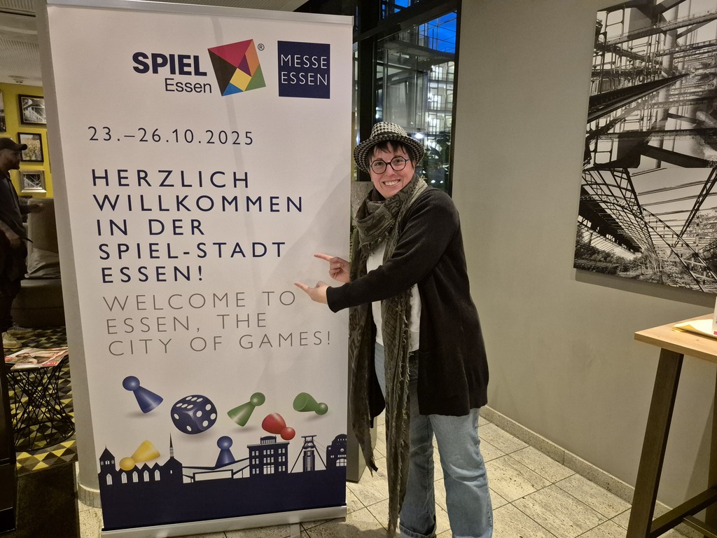 Eine Frau mit Hut steht vor einem Willkommensschild.