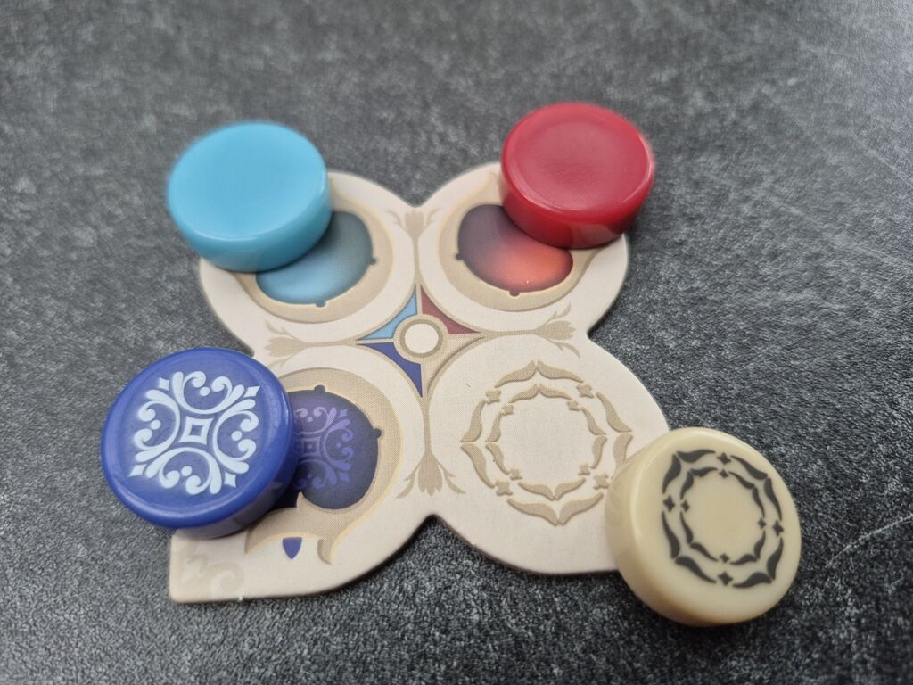 Auf einem Plättchen liegen vier runde Spielsteine.