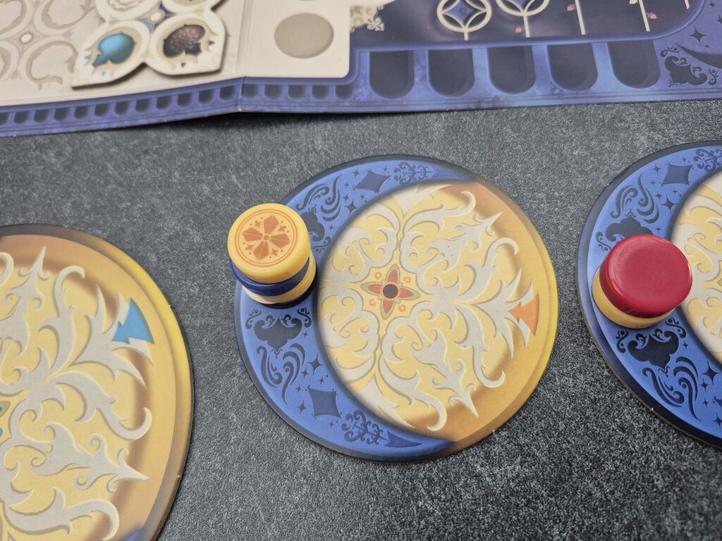 Auf zwei Plättchen liegen zwei und drei runde Spielsteine.