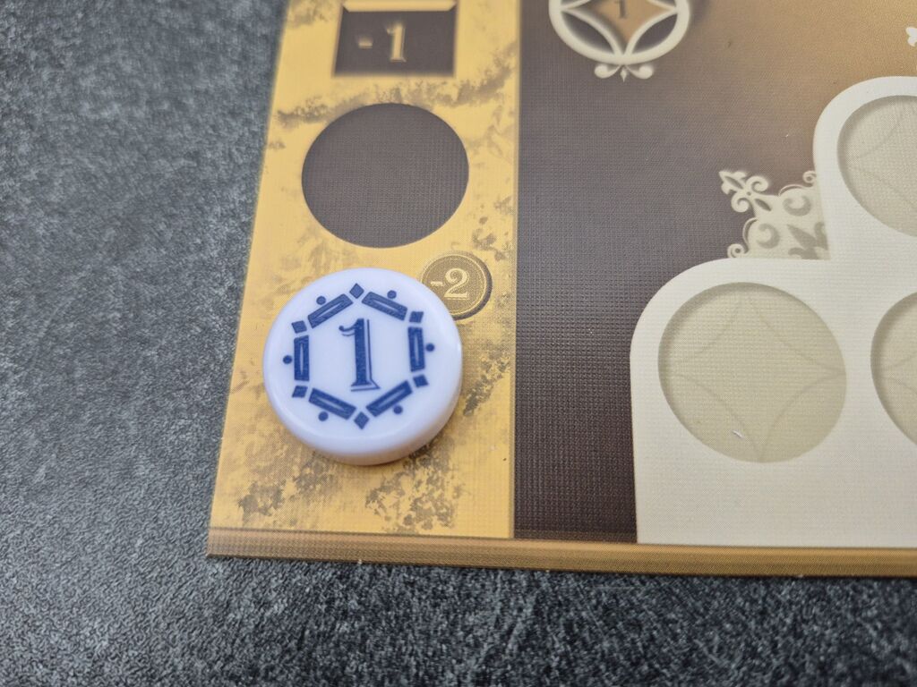Ein weißer, runder Spielstein mit einer blauen Eins liegt auf einem Spielplan.