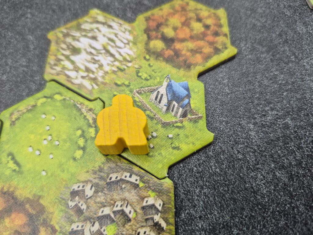 Ein gelber Meeple liegt auf einem Plättchen mit einer Kirche.