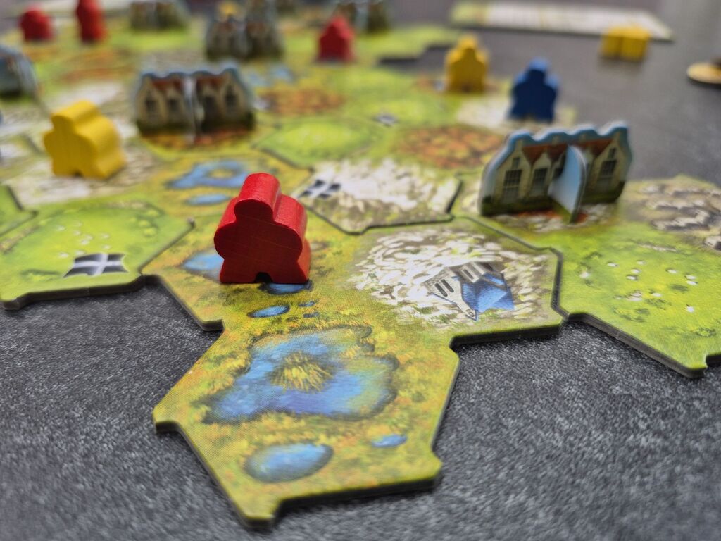 Auf dem aus Plättchen zusammengesetzten Spielplan stehen Cottages und Meeple.