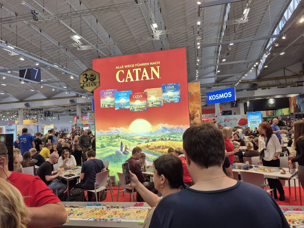 Eine große Werbewand zu "Catan", drumherum viele Menschen.