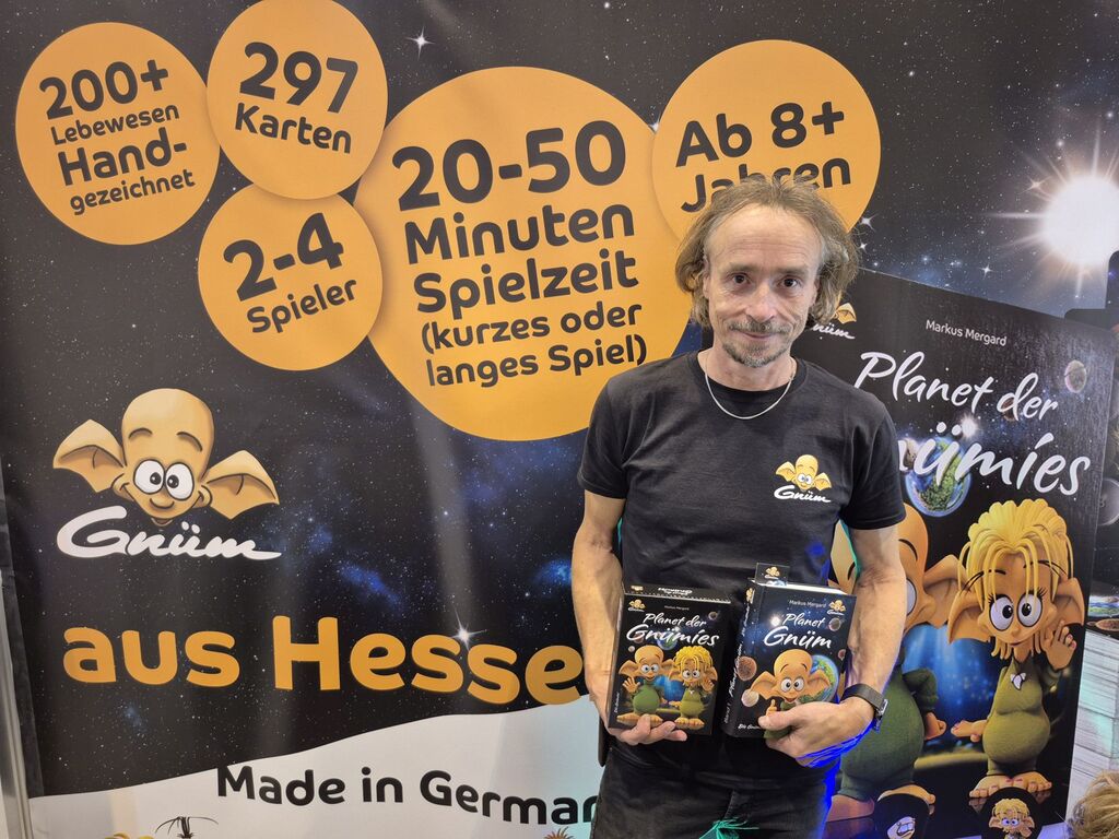 Ein Mann mit Buch und Spiel vor einer Werbewand.