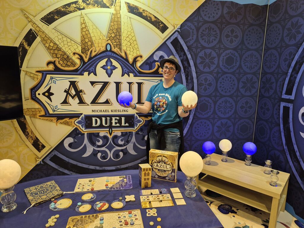 Eine Frau hält zwei leuchtende Kugeln vor einer Werbewand für "Azul Duel".