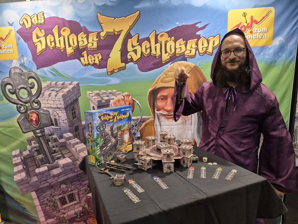 Ein Mann mit Schlüsselbund und Kutte vor Werbestand.