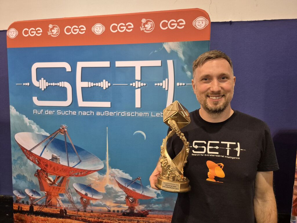 Ein Mann hält einen Pokal vor einer Werbewand für "Seti".