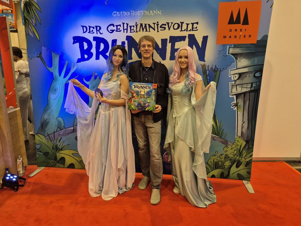 Ein Mann und zwei Frauen vor einer Werbewand.