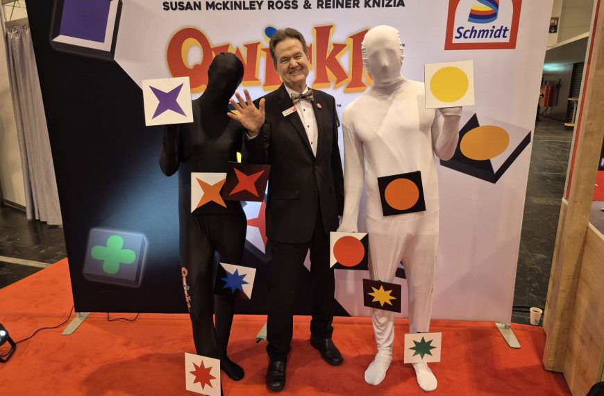 Ein Mann im Anzug, daneben zwei Personen in Overals, die auch das Gesicht bedecken.