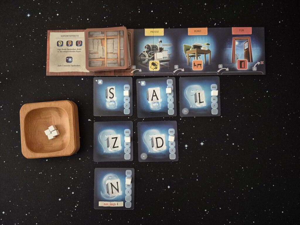 Karten mit Buchstaben und Symbolen, darüber ein kleiner Spielplan mit Symbolen und eine Schale mit weißen Holzwürfeln.