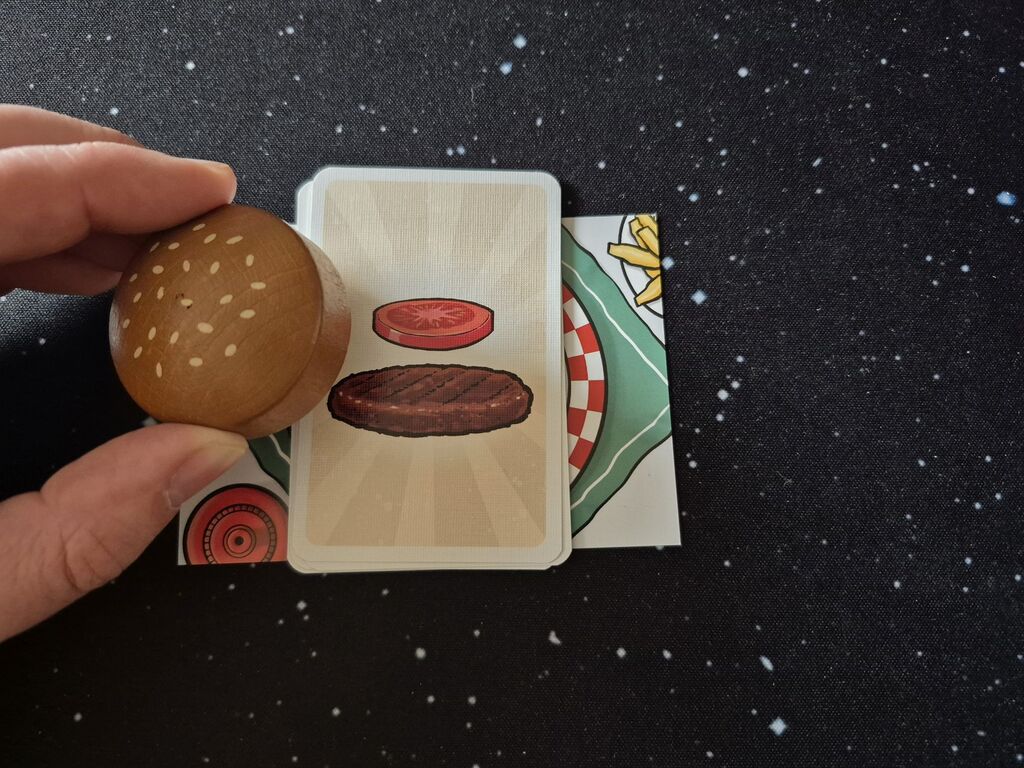 Eine Hand hält den Holzburger über einen Stapel Karten.