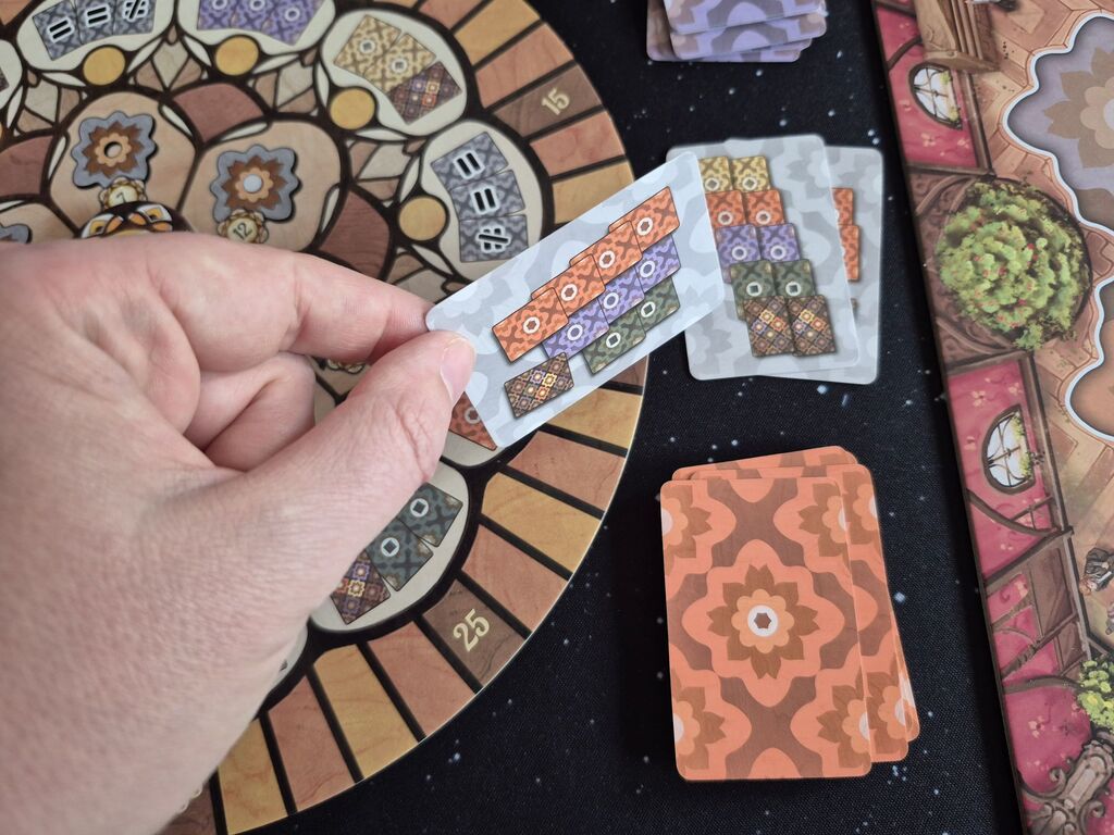 Eine Hand hält eine Karte über Spielmaterial von "Intarsia".