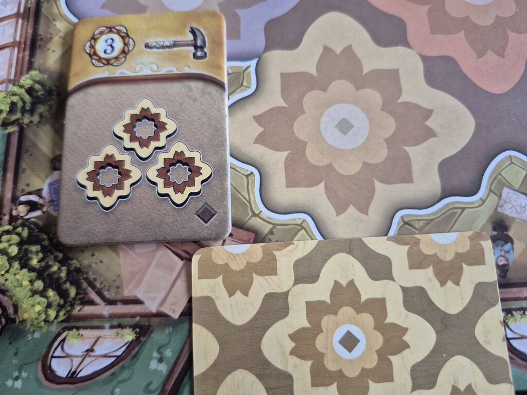 Auf Plättchen, Karte und Spielplan ist bei gelben Bauteilen eine dunkelbraune Raute zu sehen.