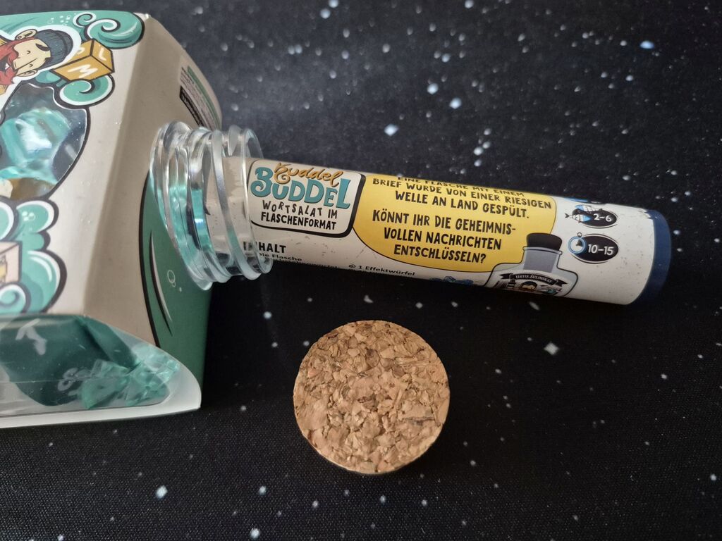 Die Anleitung von "Kuddel Buddel" ist zusammengerollt und steckt im Flaschenhals. Daneben ein Korken.