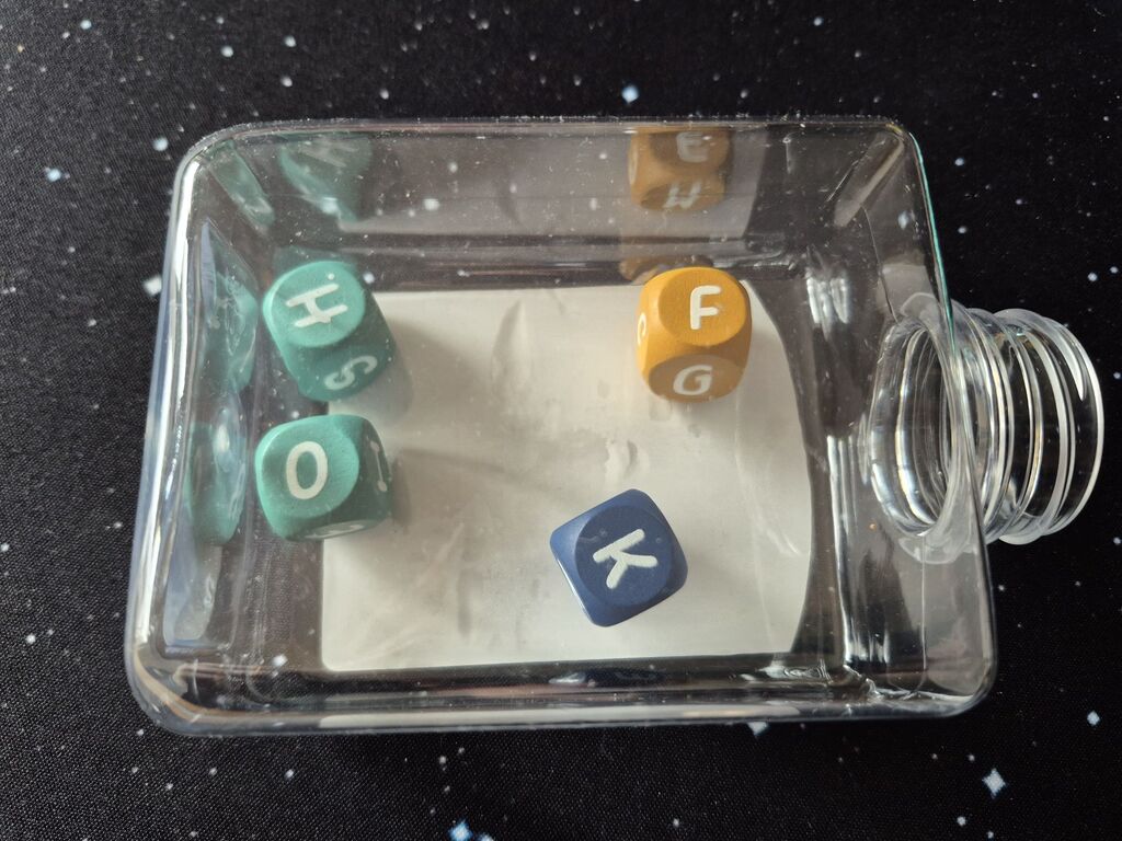 Eine Kunststoffflasche, in der vier Würfel Buchstaben zeigen.