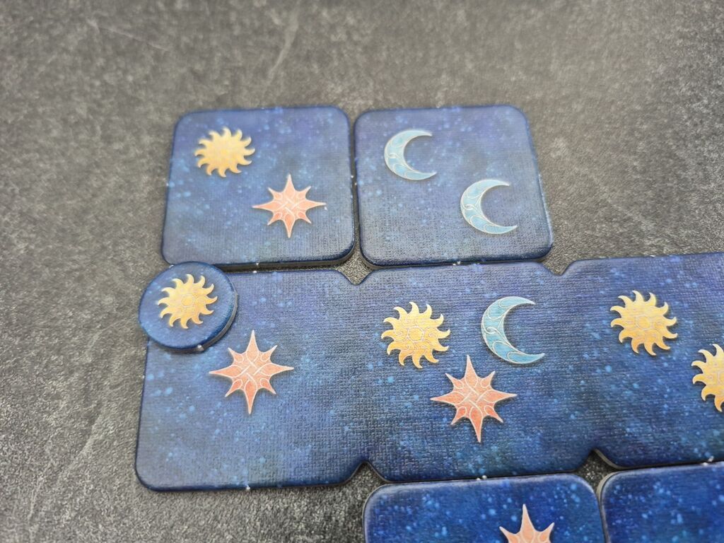 Plättchen mit zwei Sonnen, drei Monden, drei Sternen. Ein Marker mit einer Sonne.