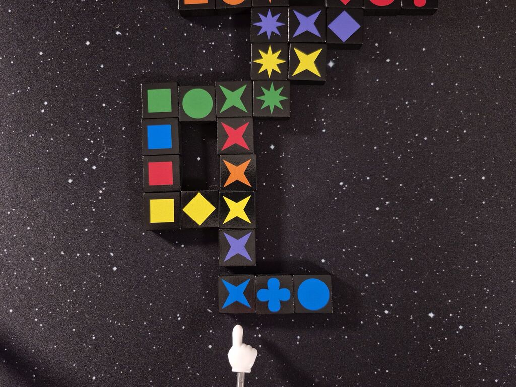 Eine Reihe blauer Steine liegt unter bereits ausliegenden Steinen von "Qwirkle".