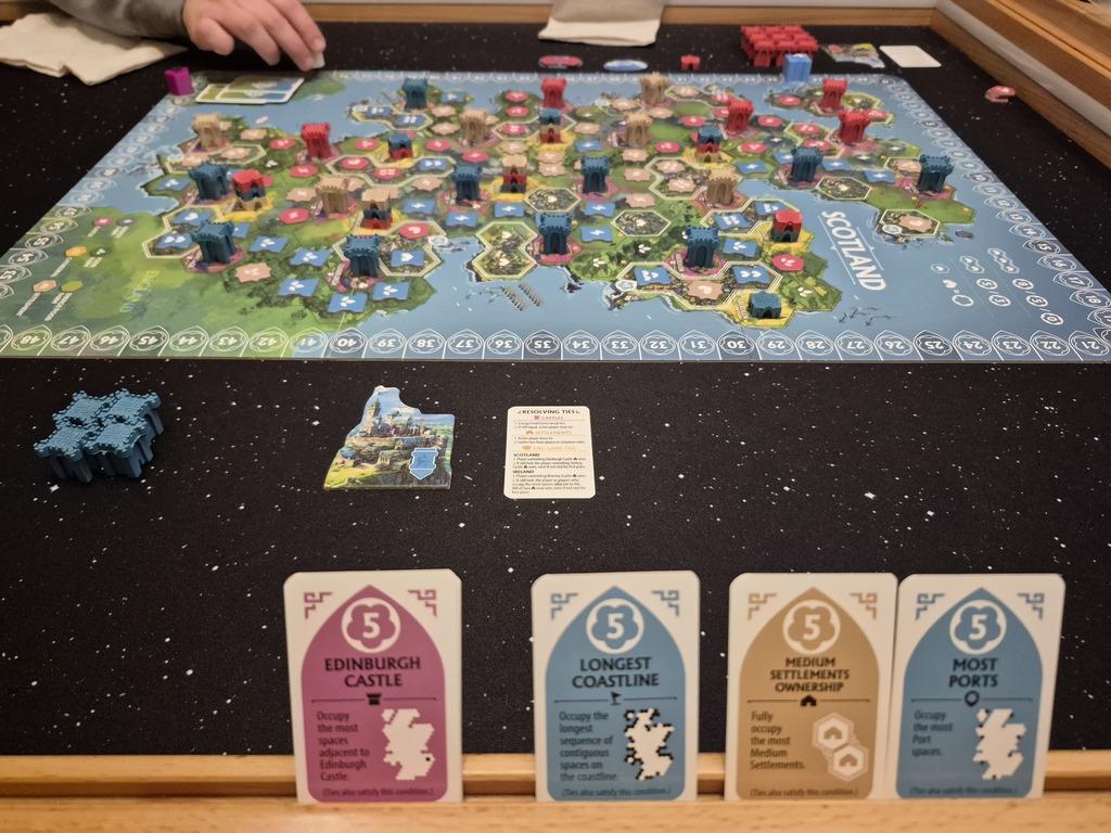 Vier Karten im Vordergrund mit Text, im Hintergrund Spielmaterial.