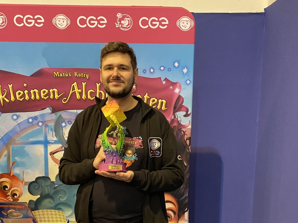 Ein Mann hält einen bunten Pokal hoch.