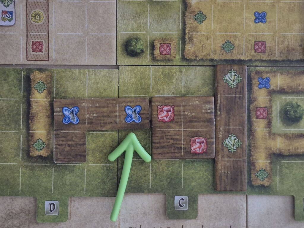 Ein Pfeil zeigt auf ein Feld auf dem Spielplan, auf dem jetzt ein Plättchen liegt.