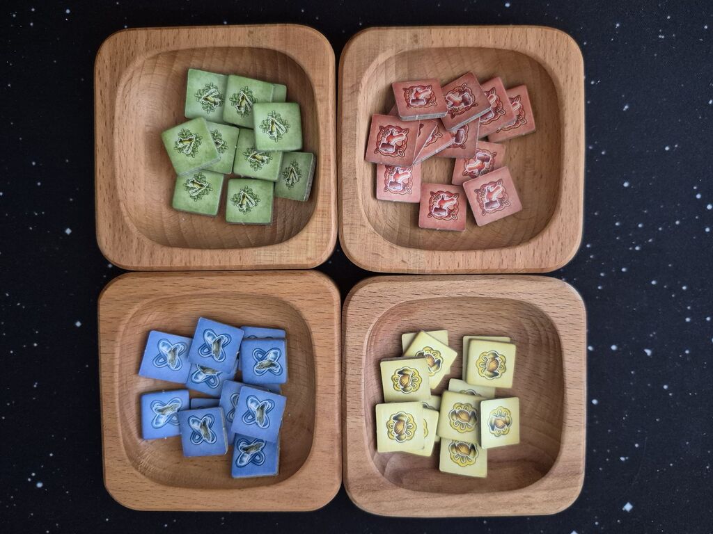 Vier Holzschalen mit quadratischen Plättchen in Rot, Gelb, Grün und Blau.