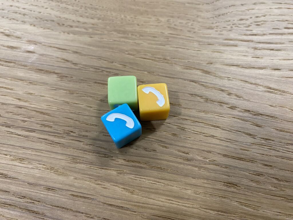 Drei Würfel in grün, gelb und blau. Zwei zeigen einen Telefonhörer.