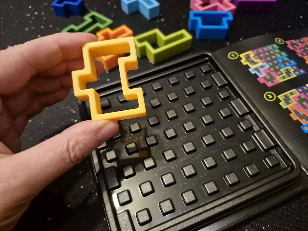 Eine Hand hält ein Teil über den Spielplan von "IQ Square".