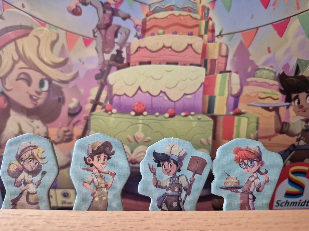 Die vier Spielfiguren aus "Topp die Torte" vor der Schachtel als Hintergrund.