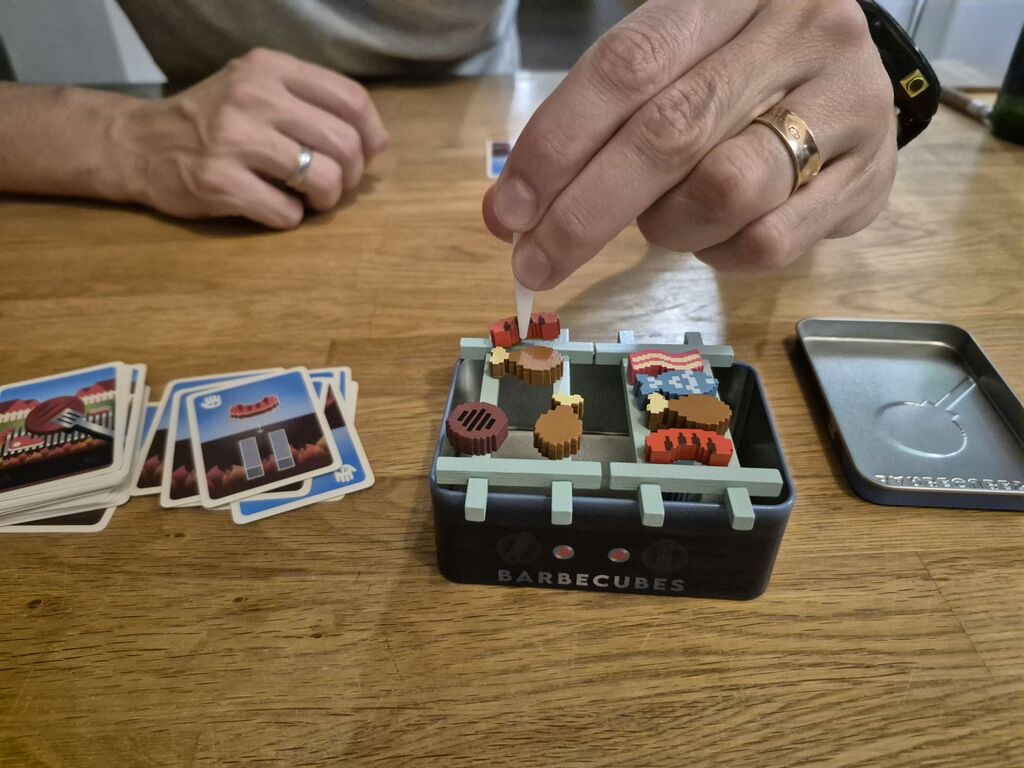 Eine Hand legt mit der "Grillzange" ein "Würstchen" auf den Rost.