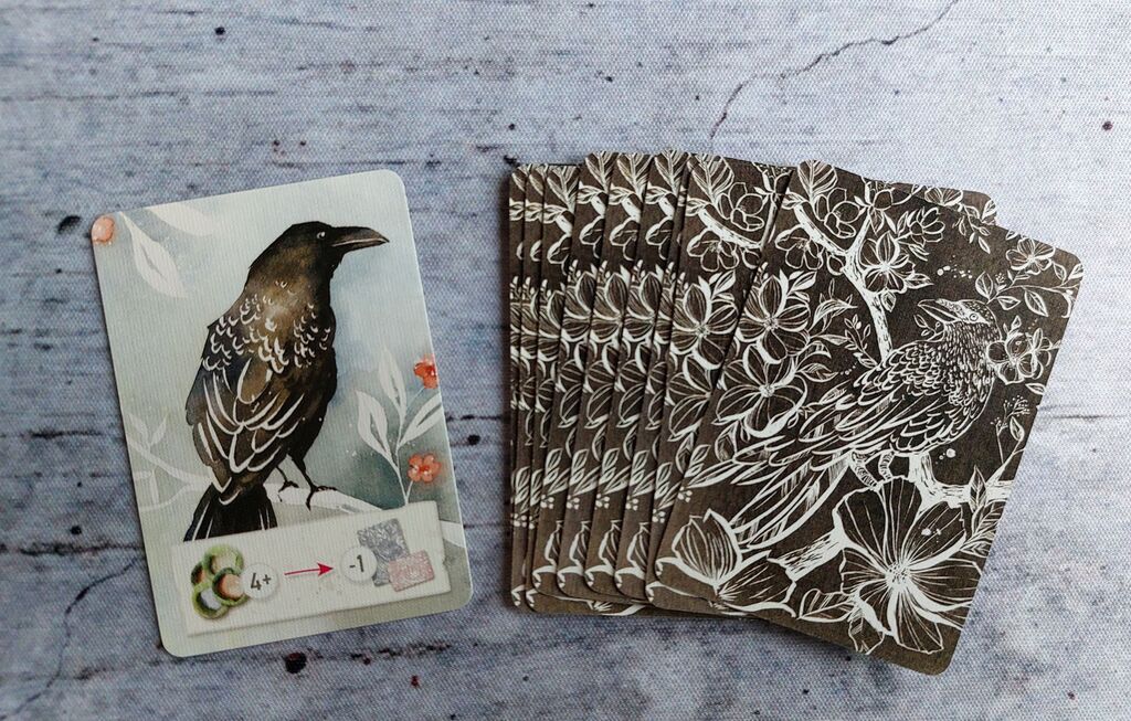 Ein Stapel schwarzer Karten, eine ist aufgedeckt und zeigt eine Krähe.