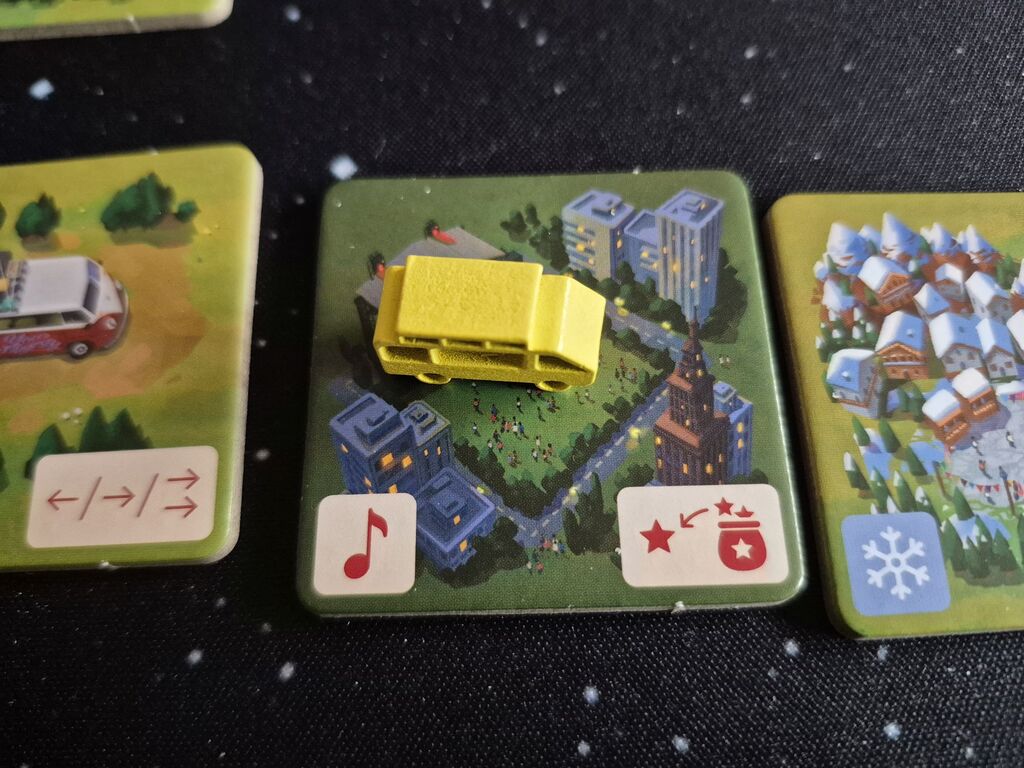 Eine Bus-Spielfigur steht auf einem Plättchen mit Symbolen.
