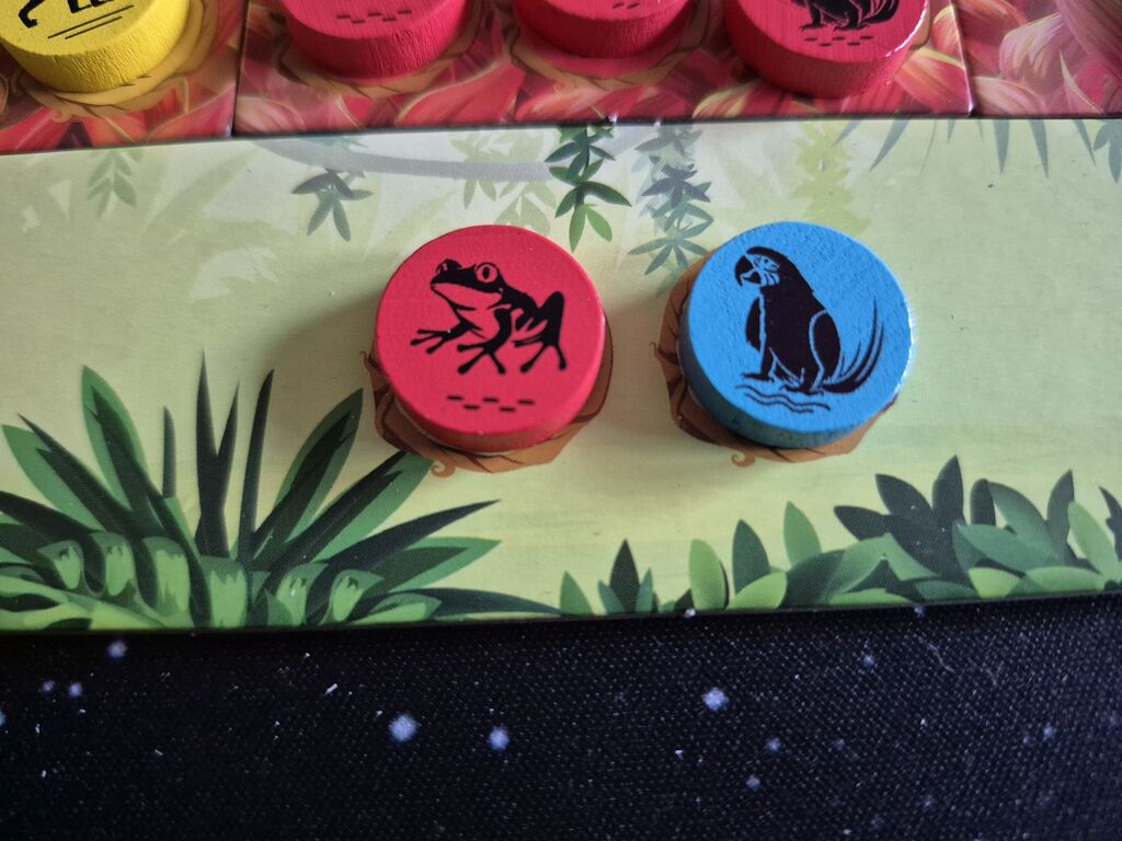 Zwei Marker liegen auf einem Tableau von "Rainforest".