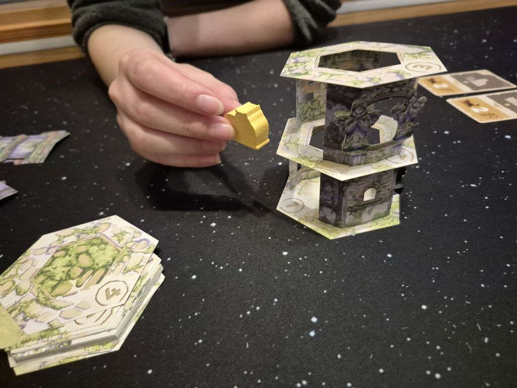 Eine Hand hält eine Katzenfigur neben den Turm.