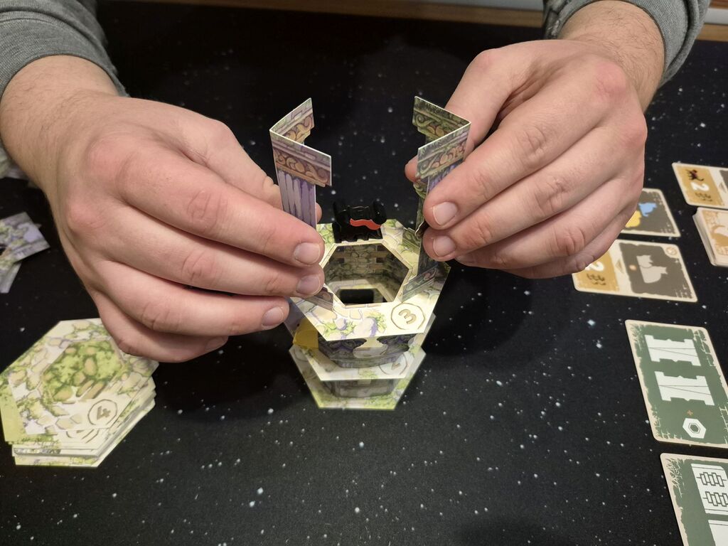 Zwei Hände halten Säulen-Bauteile über den Turm.