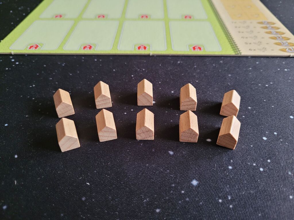 Zehn Holzhäuschen stehen vor einem Spielertableau.