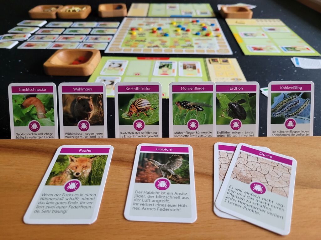 Karten zeigen Schädlinge. Dahinter das Spielmaterial von "Homefarming".