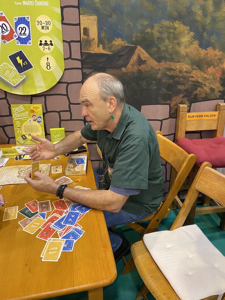 Ein Mann sitzt an einem Tisch mit vielen Karten und spricht.