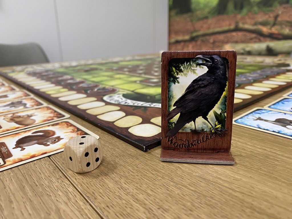 Eine Spielfigur mit einem schwarzen Raben, daneben ein Würfel und Spielmaterial von "Woodwalkers".