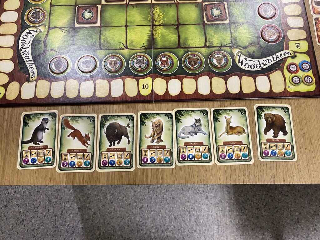 Sieben grüne Karten mit Tieren und Symbolen an einem Spielfeldrand.