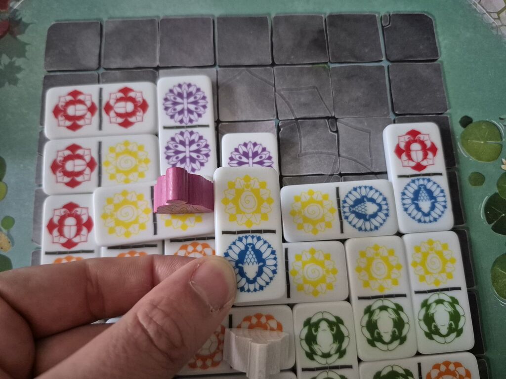 Eine Hand hält einen Spielstein über weitere Steine auf dem Spielplan von "Ananda".