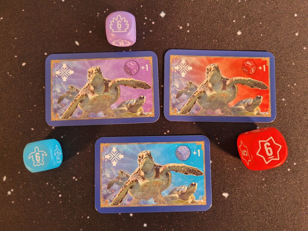 Drei Karten mit Schildkröte und Symbolen und farblich passenden Würfeln.