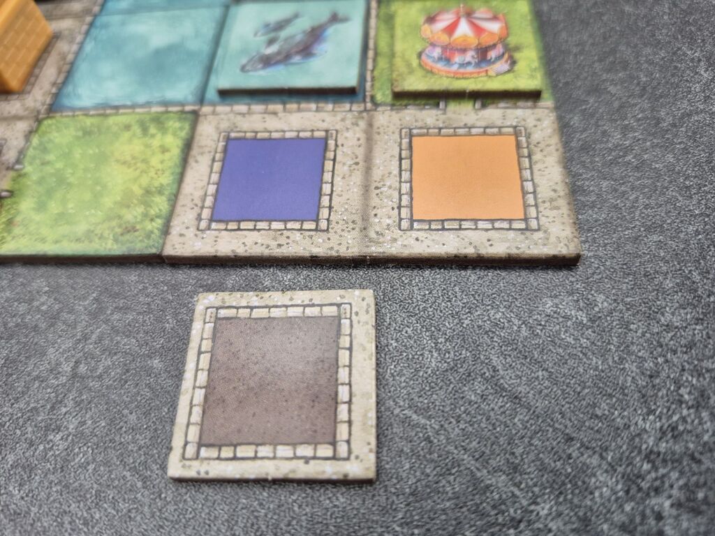 Ein Plättchen liegt neben einem Stadtplan-Teil aus "Cities".