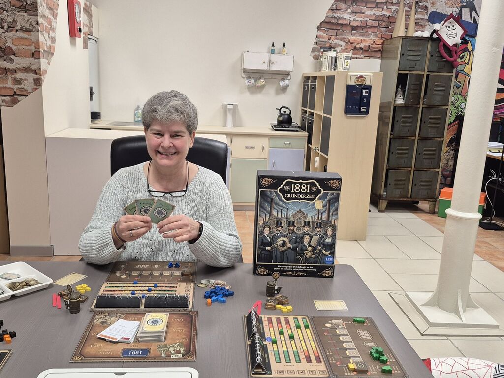 Frau sitzt an Tisch mit Spielmaterial.